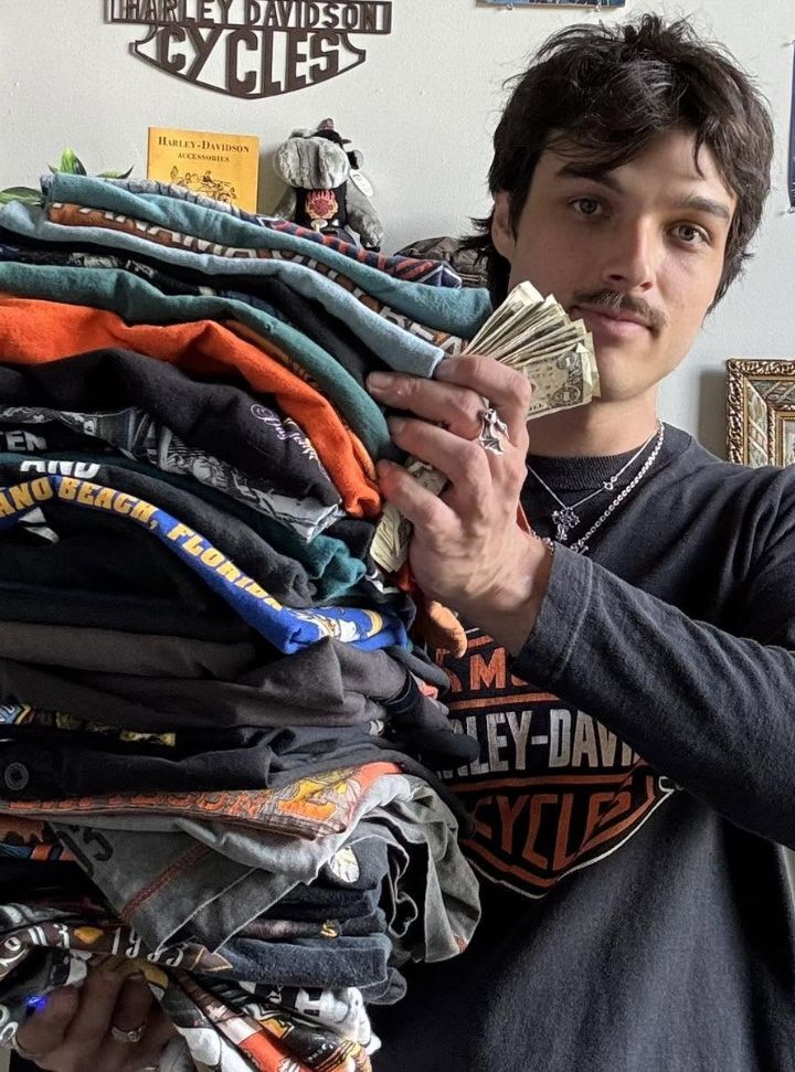 One of the two brothers behind Cash 4 Shirts, holding a tall stack of vintage T-shirts and cash